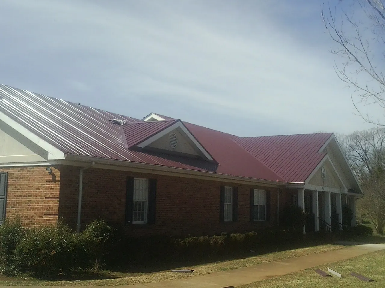 Red metal roof with gabled entries on a long brick building, from a Hail Damage Roof Repair job in Rappahannock Academy