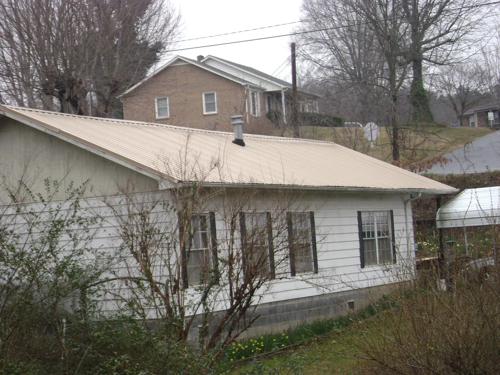 Tan metal roof on a white sided house set into a hillside — Commercial Roofing by Roofing Brothers in Rappahannock Academy
